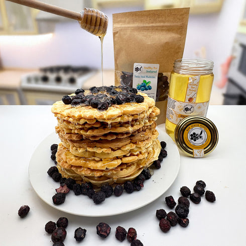 Stack of pancakes with blueberries, honey being drizzled, and a jar of honey on a table | Healthy Bee Ireland