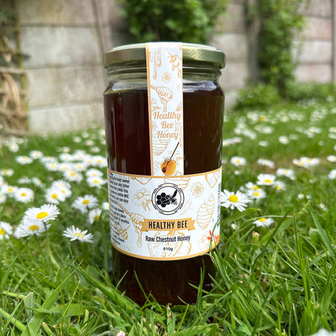 Jar of Healthy Bee Raw Chestnut Honey on grass with flowers