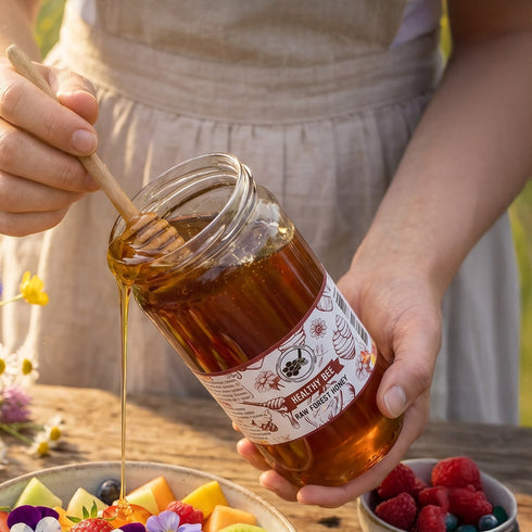 Person holding a jar of honey with a wooden dipper, surrounded by fruit and flowers | Healthy Bee Ireland